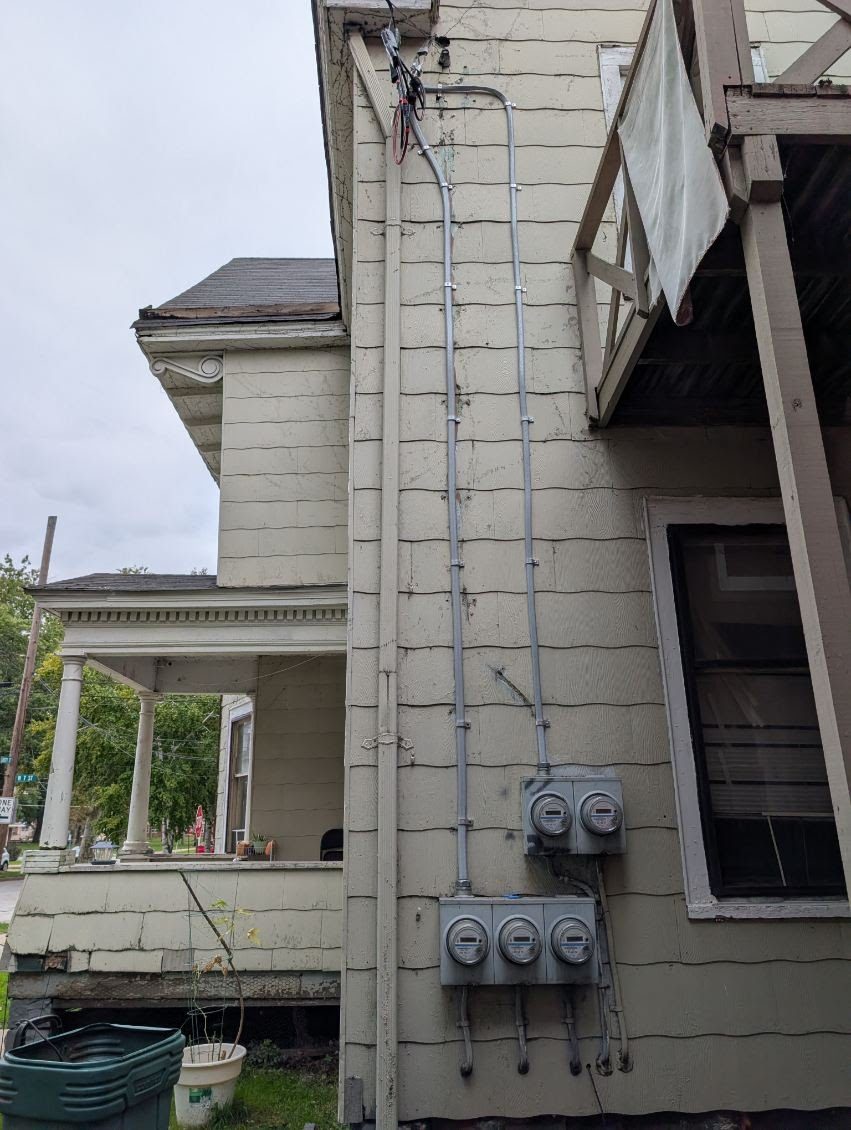 New service with five meters and conduit run up the side of a house, by VECA